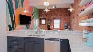 Una cocina con pared de ladrillo, una isla grande con lavavajillas y un televisor de pantalla plana montado sobre la isla.