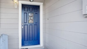 Een blauwe deur met een glas-in-loodraam, witte omlijsting en een lamp erboven.