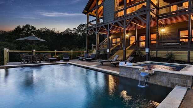 A pool with lounge chairs, a wooden deck, and a building with multiple balconies. - Toccoa Vista Pool & Spa |Mineral Bluff, GA (Mineral Bluff)