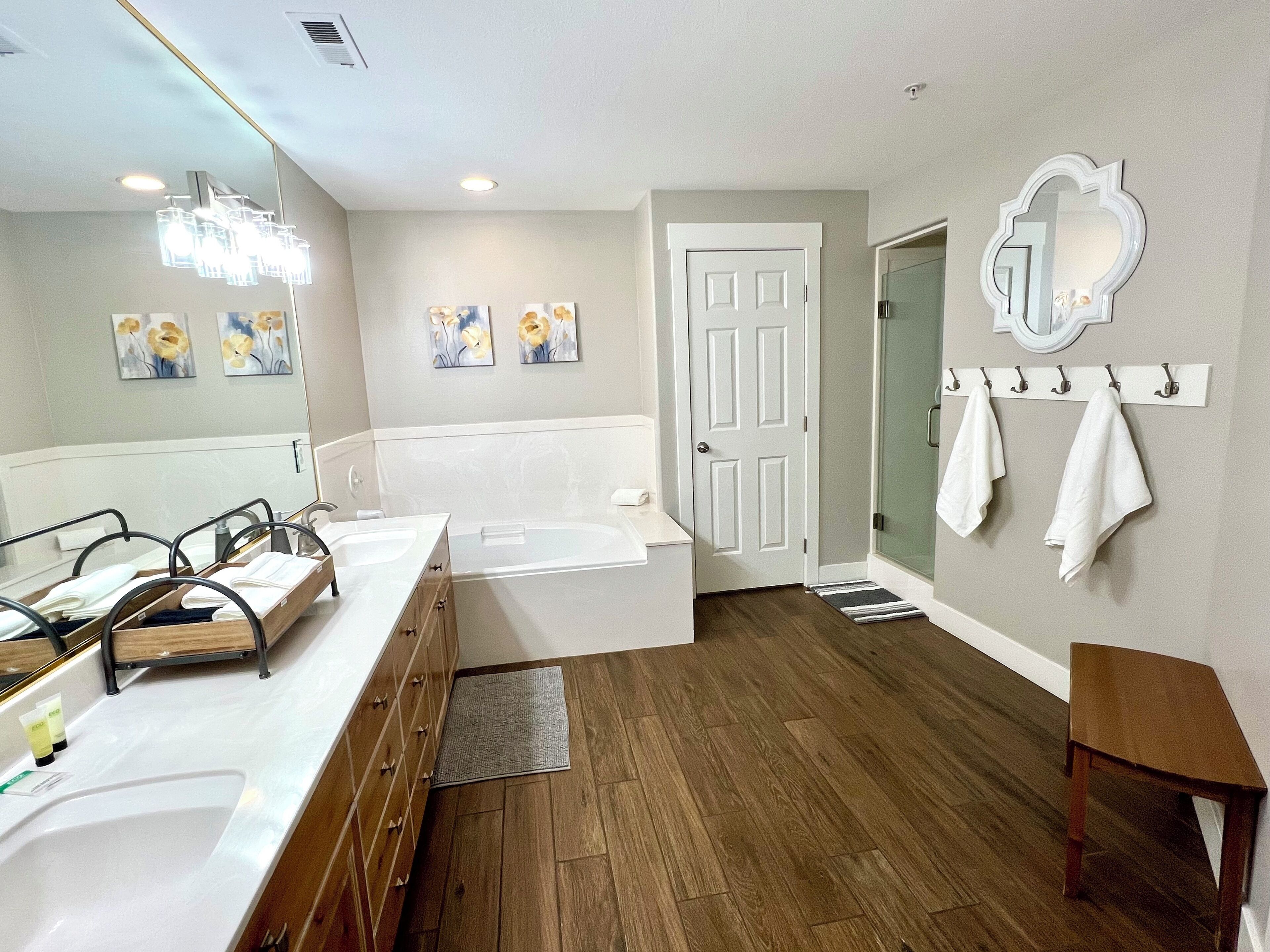 A modern bathroom with a double sink, a bathtub, and a shower. There are towels hanging on a rack and a small wooden table.