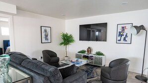 A modern living room with a grey sofa, two armchairs, a coffee table, and a TV mounted on the wall. - Stylish Downtown Apt - Workspace + Games + Parking (Dallas)