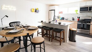 A modern kitchen with a central island, bar stools, and a dining table set for six. - Stylish Downtown Apt - Workspace + Games + Parking (Dallas)