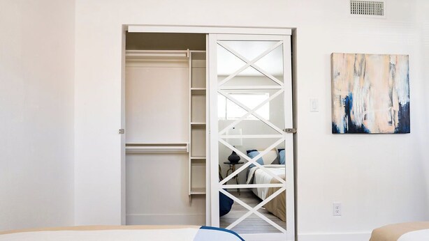A bedroom with a bed, a closet with a mirrored door, and a painting on the wall. - Stylish Downtown Apt - Workspace + Games + Parking (Dallas)