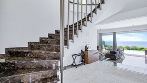 A modern interior with a marble staircase, a glass desk, and a view of the ocean. - Olymp Luxury Villa D (Kissonerga)