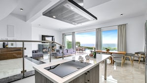A modern kitchen with a central island, a dining area with a view, and a living space with a sofa and a TV. - Olymp Luxury Villa D (Kissonerga)