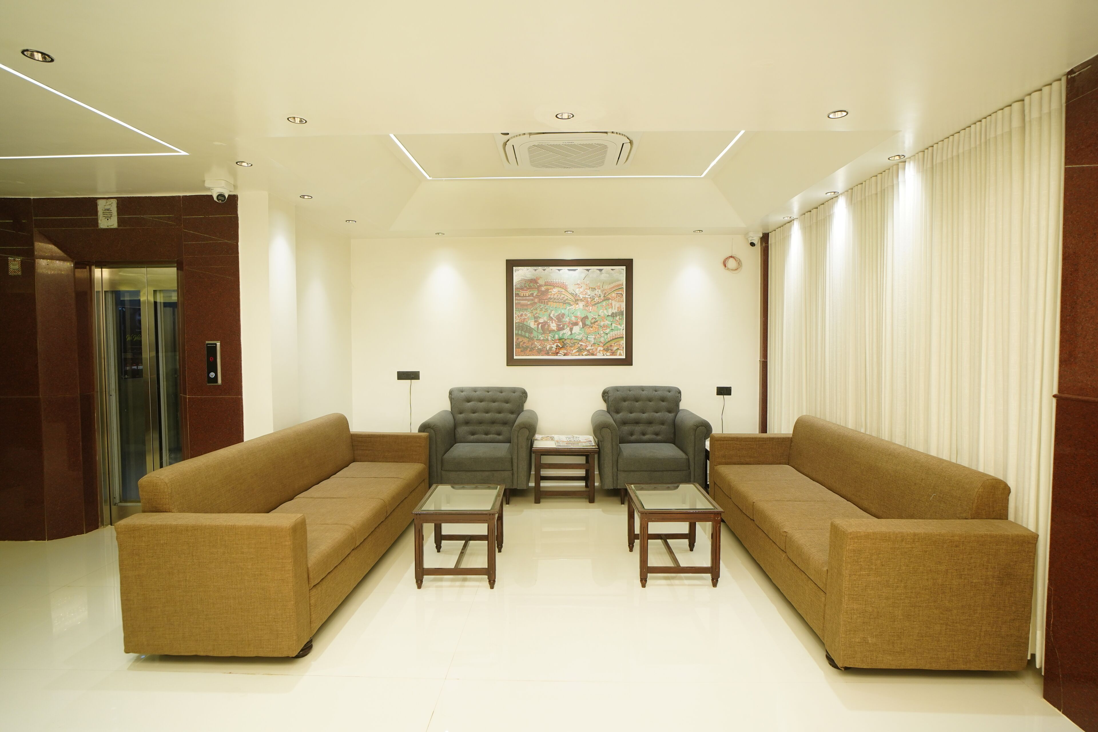 A lobby with a brown sofa, two armchairs, and a glass coffee table.