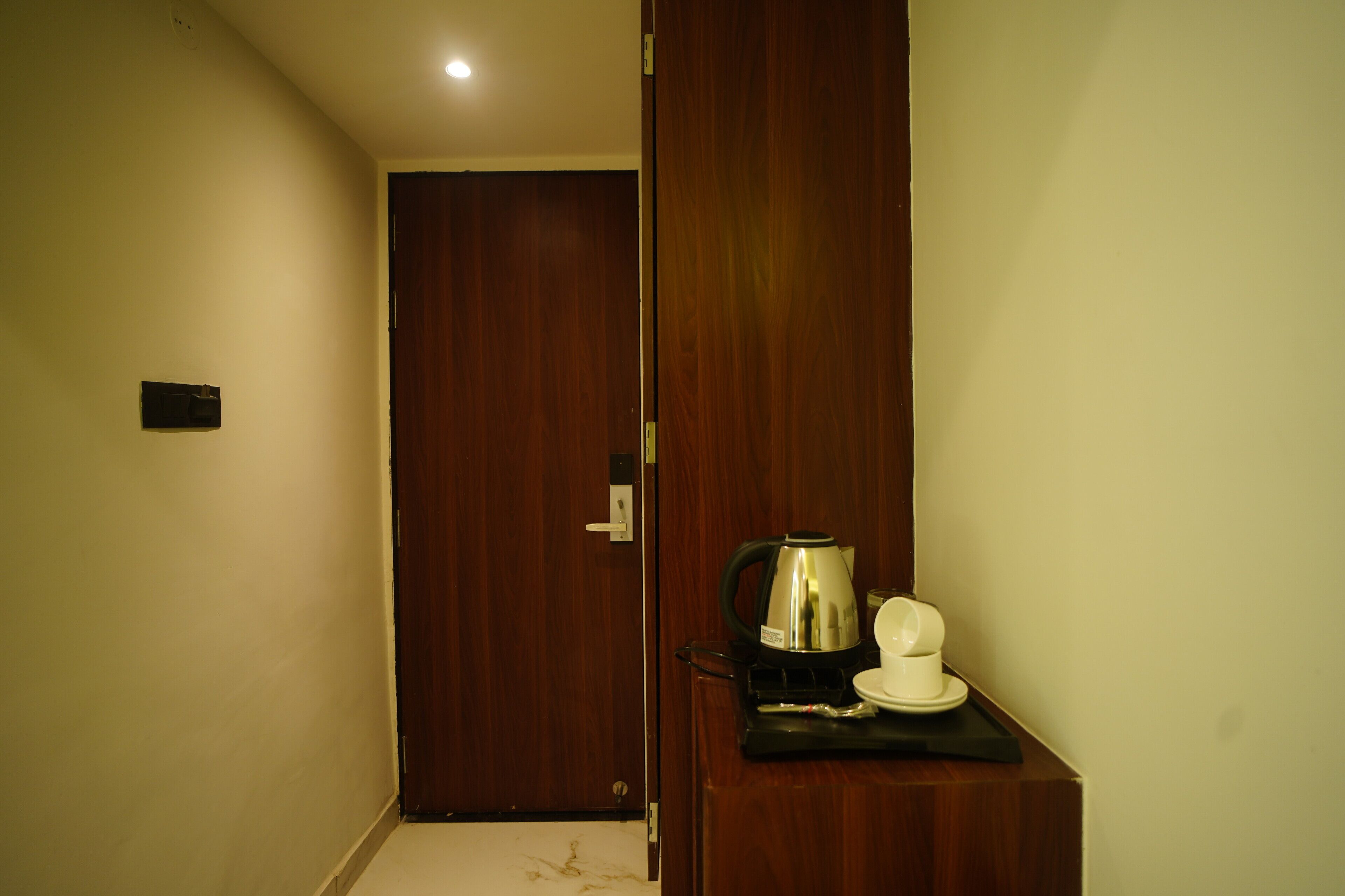 A hallway with a wooden door, a coffee maker, and a cup on a tray.