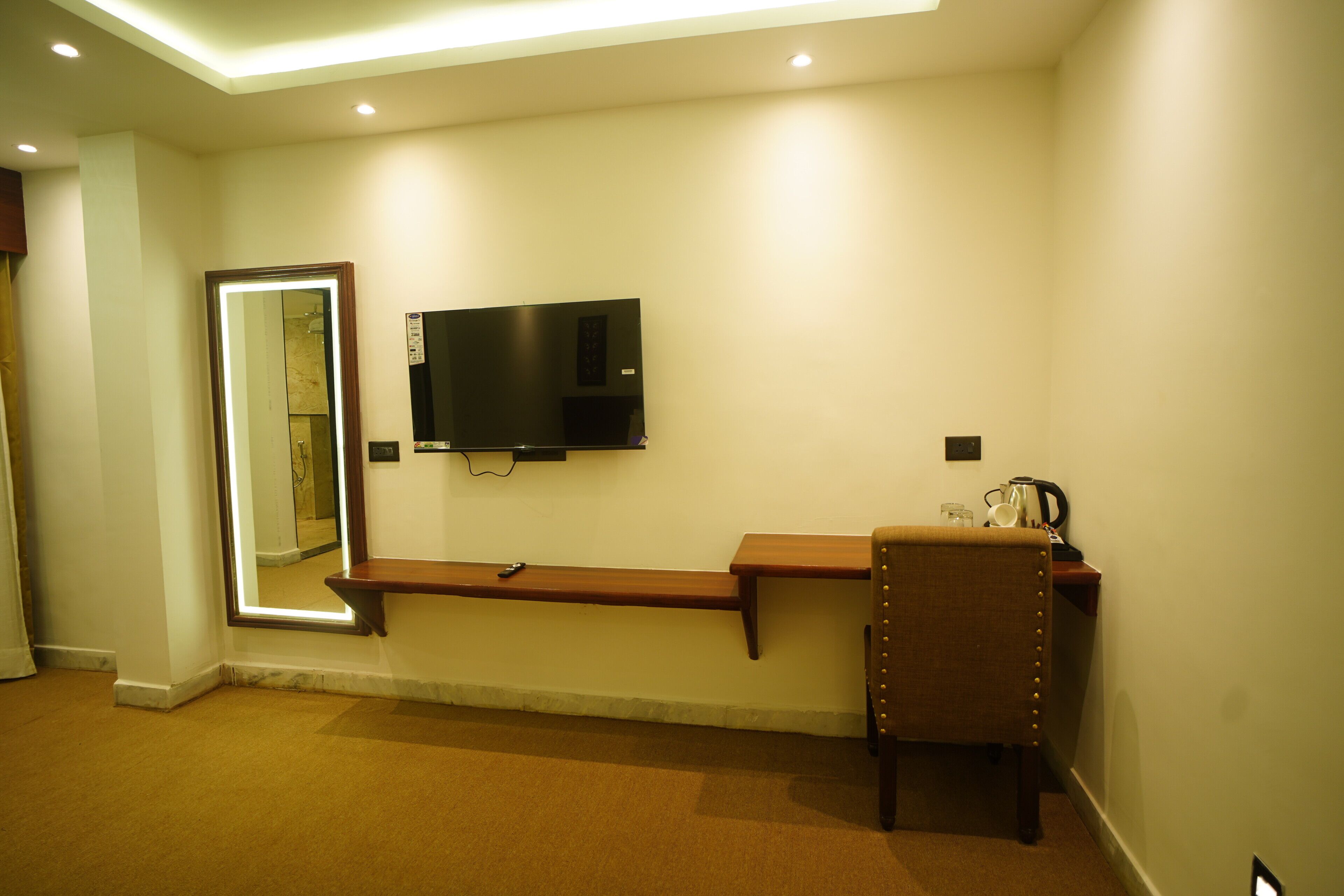 A hotel room with a flat-screen TV mounted on the wall, a wooden bench, and a chair.