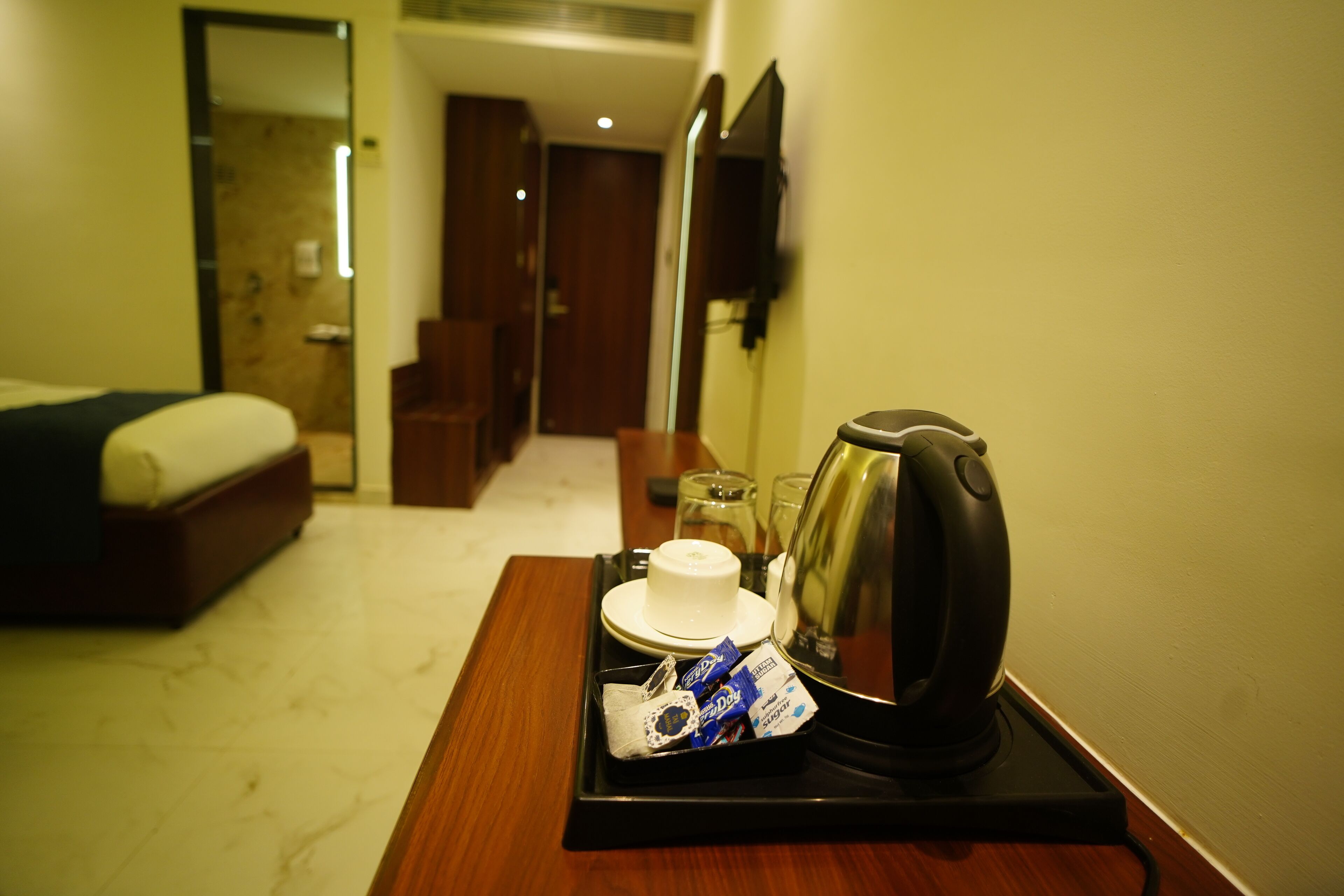 A hotel room with a bed, a bedside table with a kettle, cups, and snacks.