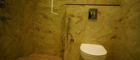 A bathroom with a marble floor, a toilet, and a shower area with a glass door.