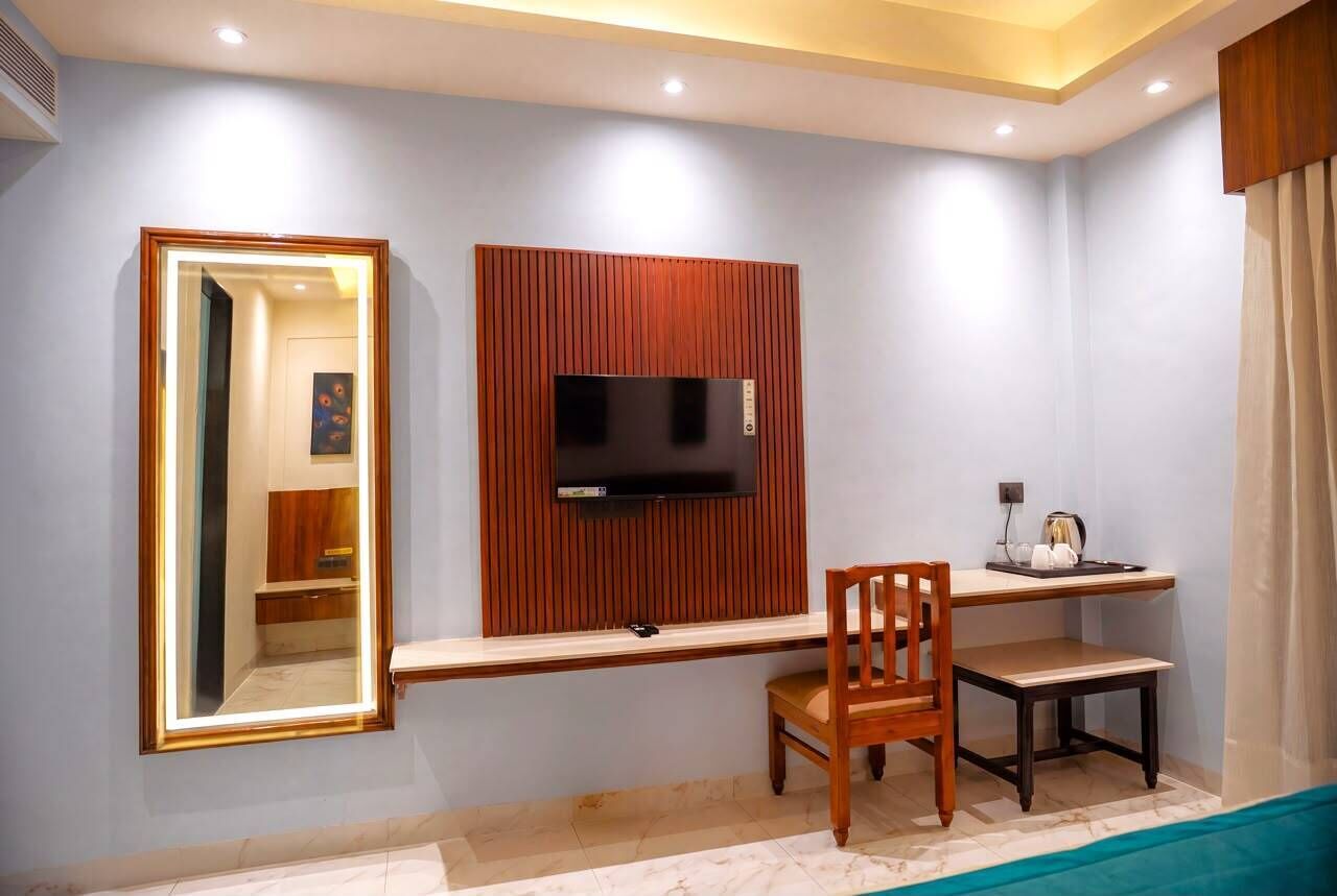 A room with a TV mounted on a wooden panel, a desk with a chair, and a large mirror.