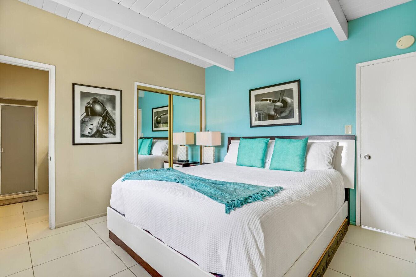 A hotel room with a large bed, teal walls, and framed artwork on the walls.