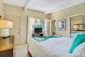 Une chambre à coucher comprenant un lit, une télévision, un bureau avec une lampe, un miroir et une fenêtre avec des rideaux.