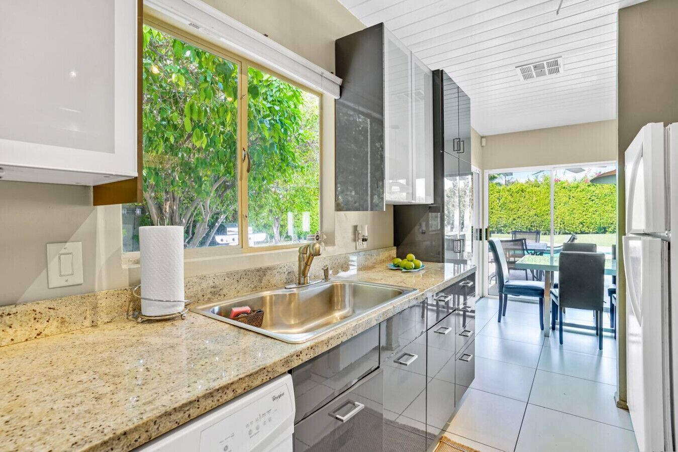 A modern kitchen with granite countertops, stainless steel appliances, and a large window overlooking greenery.
