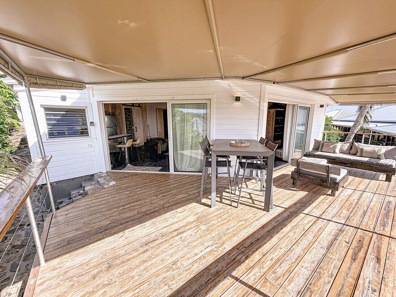 A covered outdoor deck with a wooden floor, a table with chairs, and a sofa.