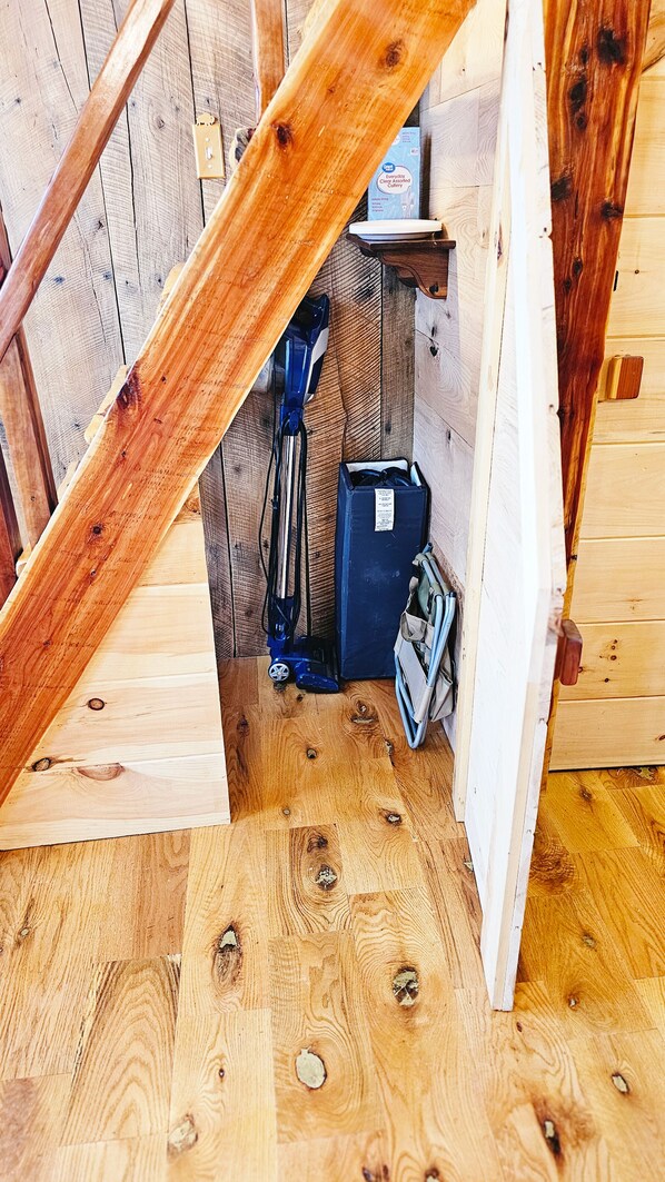 A wooden staircase leading to a loft area with a blue vacuum cleaner and a box labeled 'Everyday Clear Absorbed Cutter' on a shelf.
