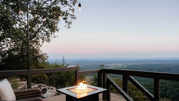 Eine Terrasse mit Feuerstelle, Korbmöbeln und Blick auf die Landschaft.