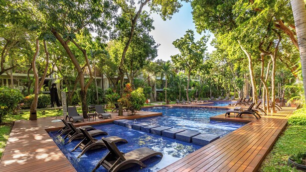 A pool area with wooden deck, lounge chairs, and a hot tub.
