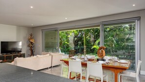 A modern living room with a flat-screen TV, a sofa, and a dining area with a glass table and chairs.