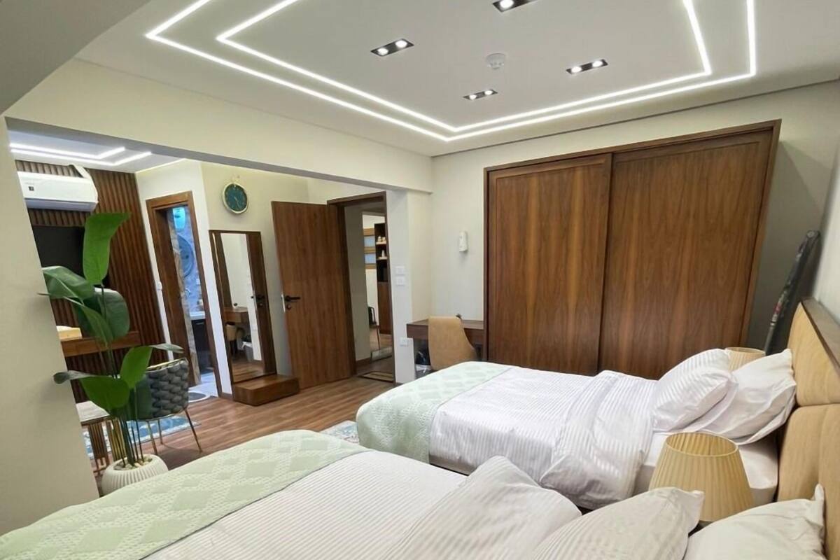 A modern bedroom with a large bed, a wooden wardrobe, and a ceiling with recessed lighting.