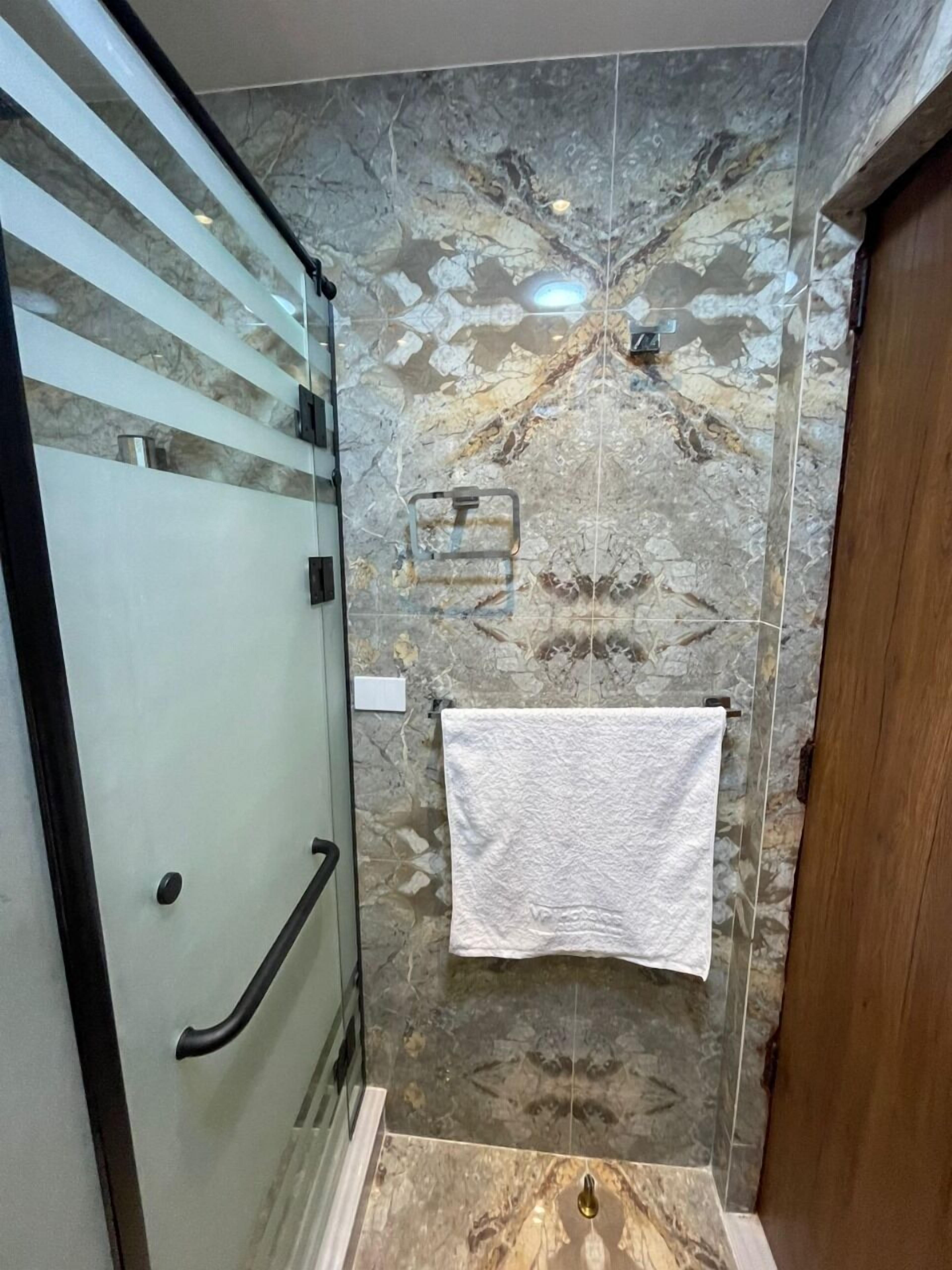 A bathroom with a glass shower enclosure, a marble-patterned wall, and a wooden door.