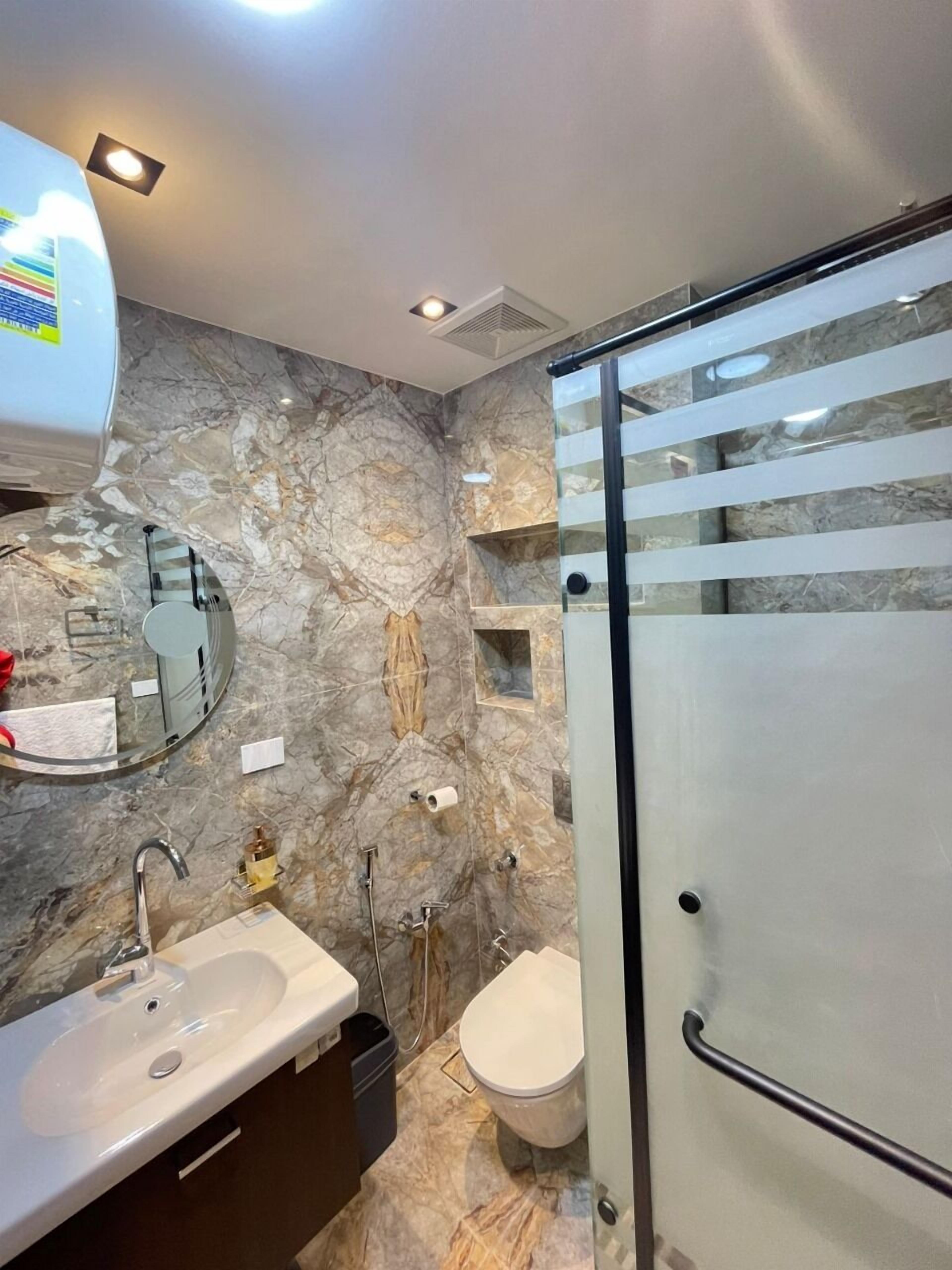 Un baño moderno con salpicadero de mármol, cabina de ducha de vidrio, lavabo con grifo y un inodoro.