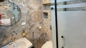 Un baño moderno con salpicadero de mármol, cabina de ducha de vidrio, lavabo con grifo y un inodoro.