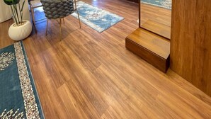 Une chambre d’hôtel moderne avec un plancher en bois, un grand miroir, un lit, une tél évision et un coin salon comprenant une chaise et une plante.