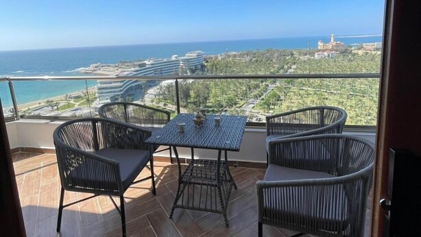 Un balcon avec une table et des chaises, offrant une vue sur la mer et les bâtiments situés au loin.