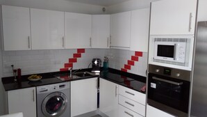 A compact kitchen with white cabinets, a washing machine, a microwave, and a sink. - Puerta del Sol, fully equipped apartment, ideally located close to all amenities (Caleta de Fuste)