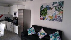 A modern kitchen with white cabinets, a stainless steel refrigerator, and a microwave. There is a black sofa with floral cushions and a tropical-themed painting on the wall. - Puerta del Sol, fully equipped apartment, ideally located close to all amenities (Caleta de Fuste)