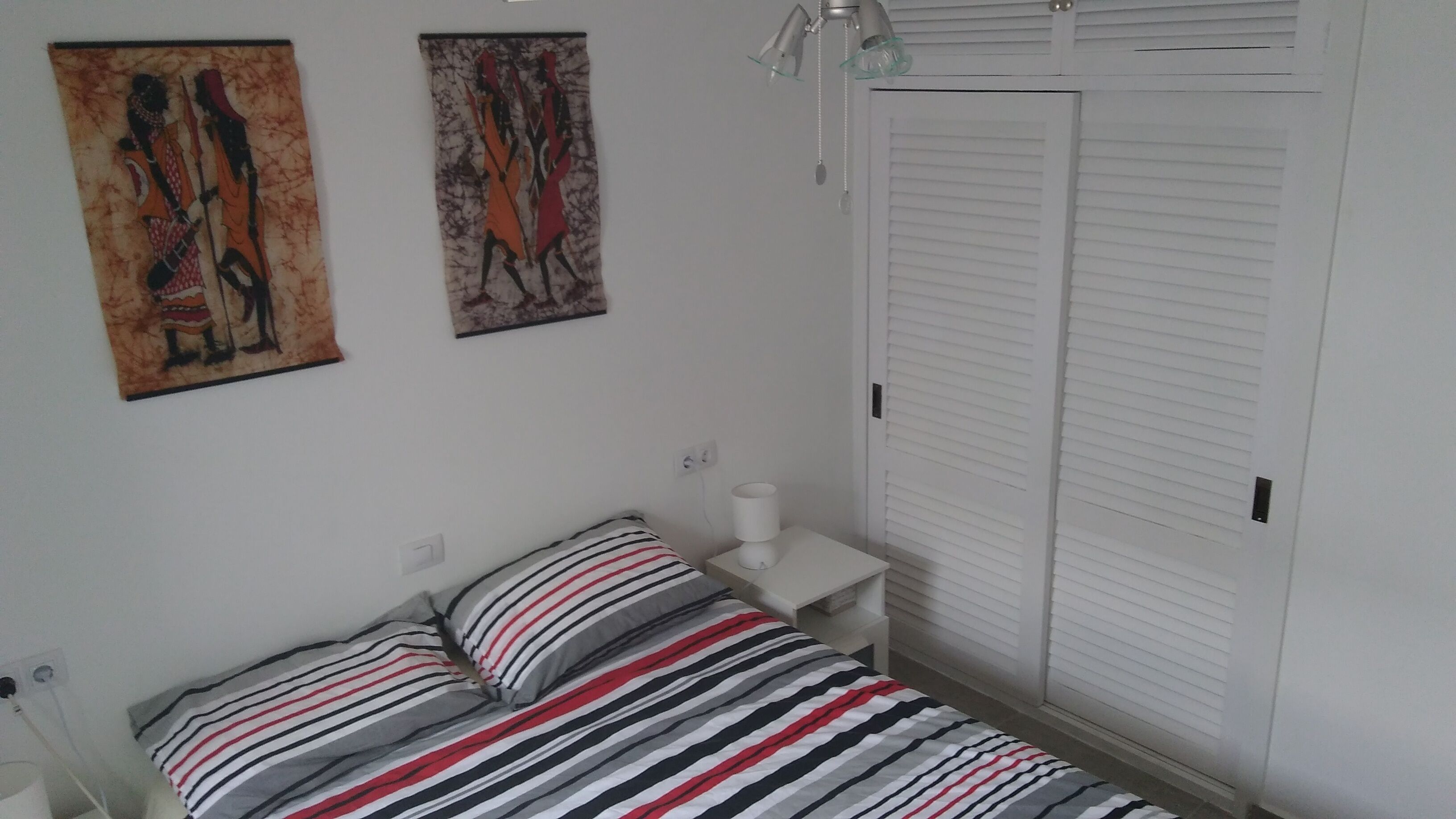 A bedroom with a bed, a bedside table with a lamp, and a wardrobe.