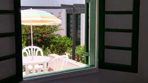 An open window with a view of a patio area, including a table, chairs, and a colorful umbrella. - Puerta del Sol, fully equipped apartment, ideally located close to all amenities (Caleta de Fuste)