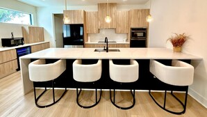 Una cocina moderna con una isla central, taburetes de bar, iluminación colgante y armarios de madera.