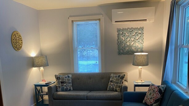 Un salon avec un canapé gris, un fauteuil bleu, un tapis à motifs et deux tables d’appoint avec des lampes.