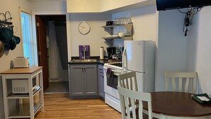 Une cuisine de taille réduite avec un coin repas, un ventilateur de plafond, une horloge et un téléviseur fixé au mur.