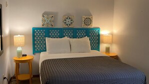 Une chambre à coucher avec un grand lit, deux lampes de chevet, une petite table de nuit en bois et des œuvres d’art décoratives accrochées au mur.