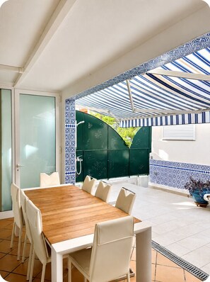 Un comedor con mesa de madera y sillas blancas, una puerta verde y un papel tapiz estampado.