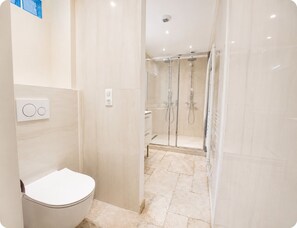 A modern bathroom with a toilet, a shower enclosure, and a wall-mounted thermostat.