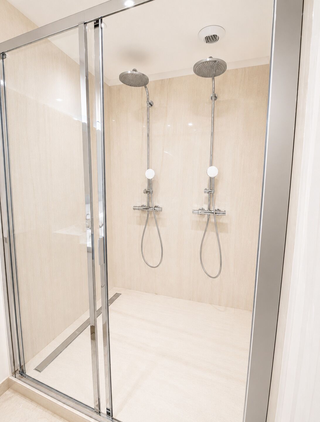 A glass-enclosed shower area with two overhead showerheads and a control panel.