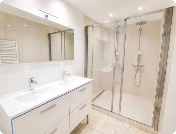 A modern bathroom with a glass-enclosed shower, a white vanity with two sinks, and a large mirror above the vanity.