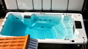 A hot tub with a clear blue pool, a ladder, and a sun lounger.