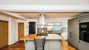 A modern kitchen with a central island, stainless steel appliances, and a large window providing natural light. - South Downs Retreat (Sompting)