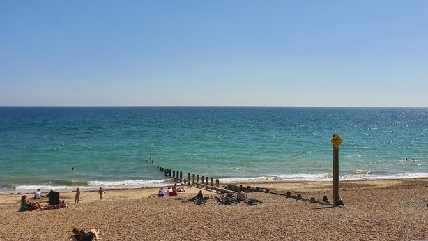 A pebbled beach with a wooden pier extending into the sea, people relaxing on the sand, and a clear blue sky. - South Downs Retreat (Sompting)