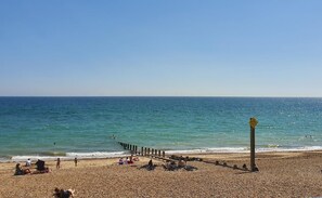 A pebbled beach with a wooden pier extending into the sea, people relaxing on the sand, and a clear blue sky. - South Downs Retreat (Sompting)