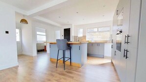A modern kitchen with a central island, bar stools, and grey cabinets. - South Downs Retreat (Sompting)