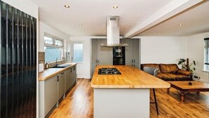 A modern kitchen with a central island, built-in appliances, and a dining area with a brown leather sofa. - South Downs Retreat (Sompting)