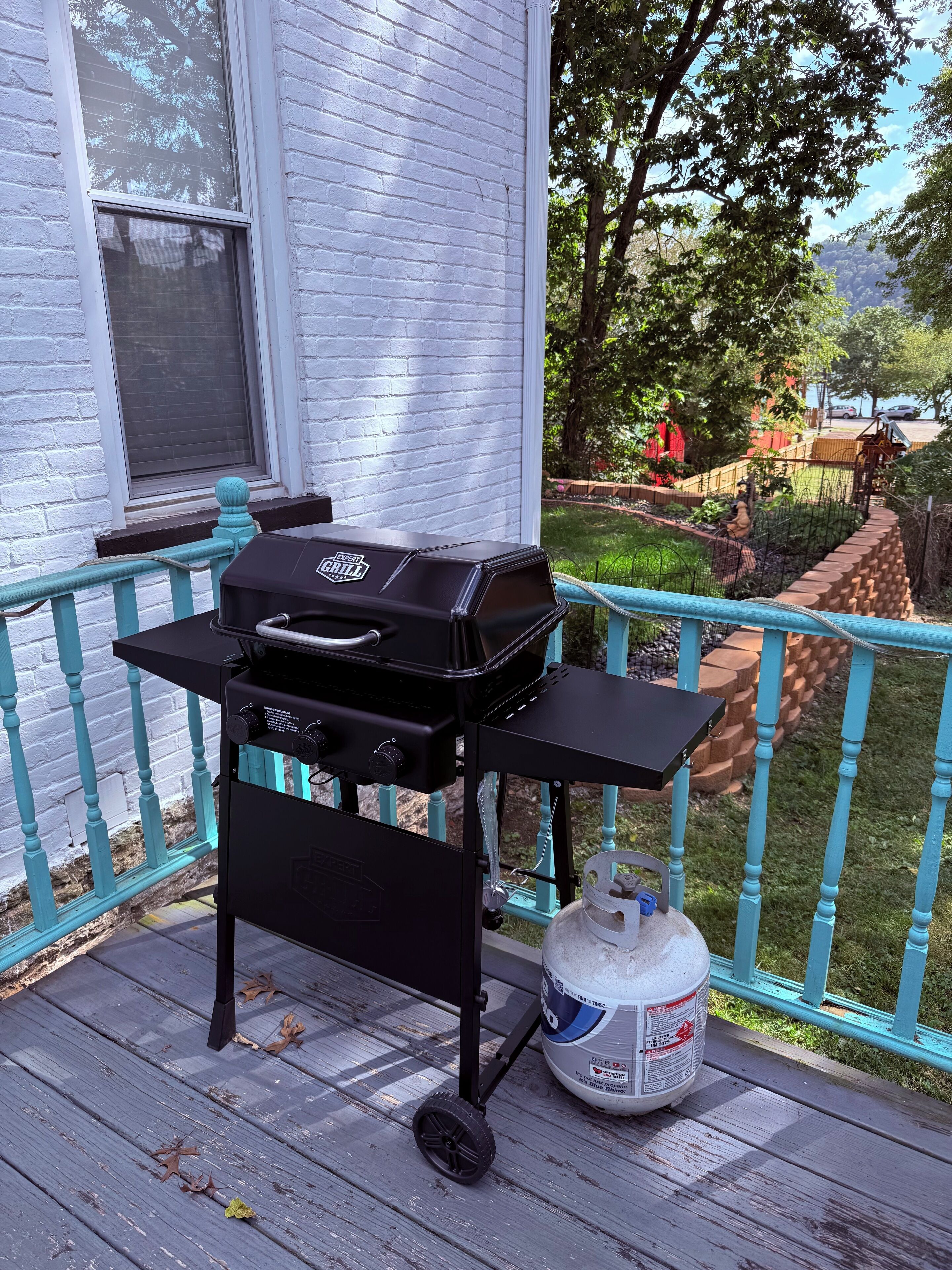 A barbecue grill on a porch with a gas tank nearby.