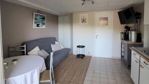 A compact room with a bed, a small table, a kitchenette, and a door with artwork. - Charming 35 m2 apartment with terrace and garden (Domont)