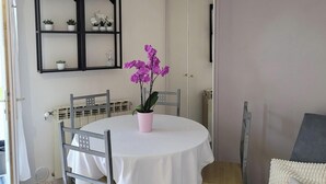 A dining area with a round table, chairs, and a potted orchid. There is a shelf with plants and a radiator. - Charming 35 m2 apartment with terrace and garden (Domont)